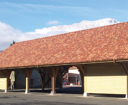 Zadaszenie z dachówką karpiówką w odcieniach czerwieni i brązu, drewniana konstrukcja nośna, w tle góra ze śnieżnym szczytem pod błękitnym niebem.