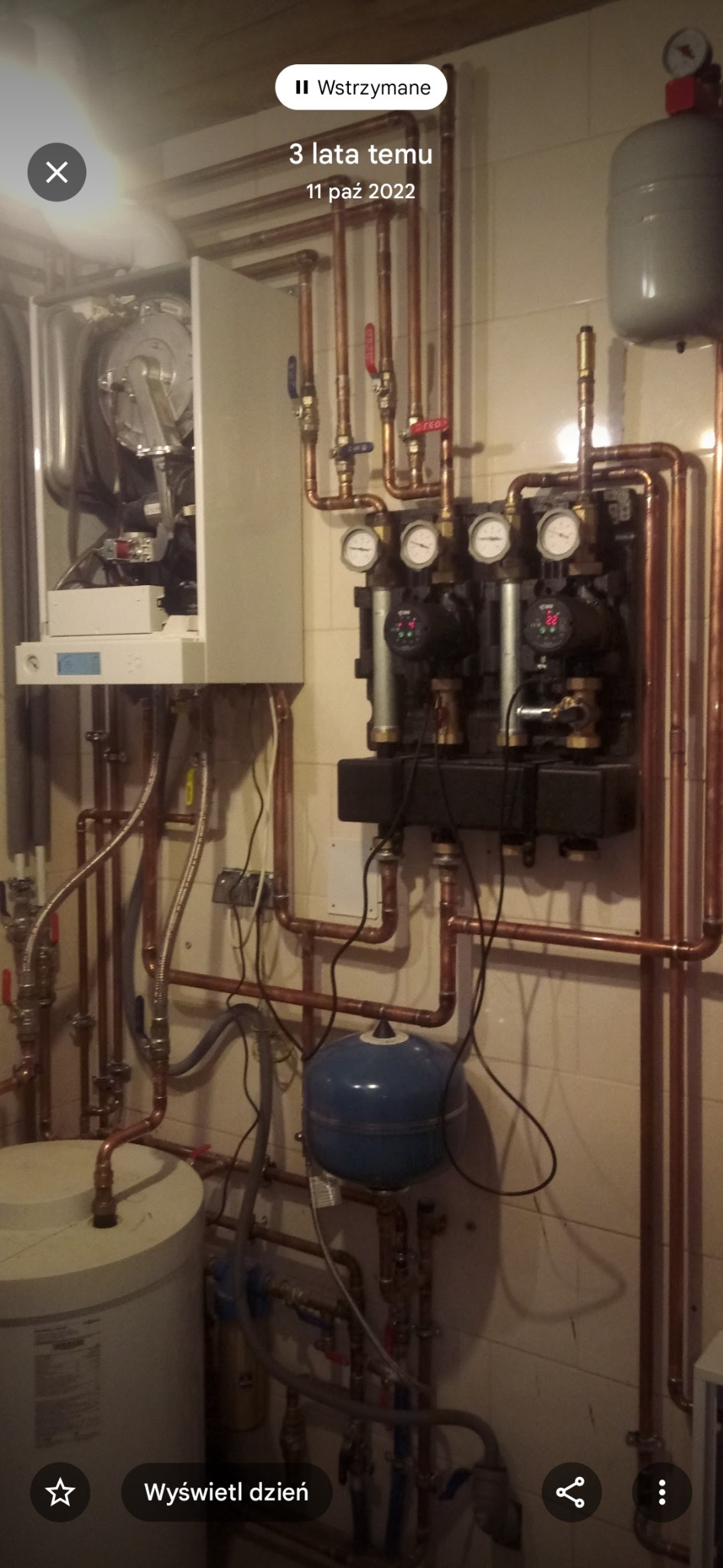 Złożona instalacja grzewcza z kotłem, pompami obiegowymi i zbiornikiem wyrównawczym. Miedziane rury łączą elementy w system, widoczne manometry i zawory.