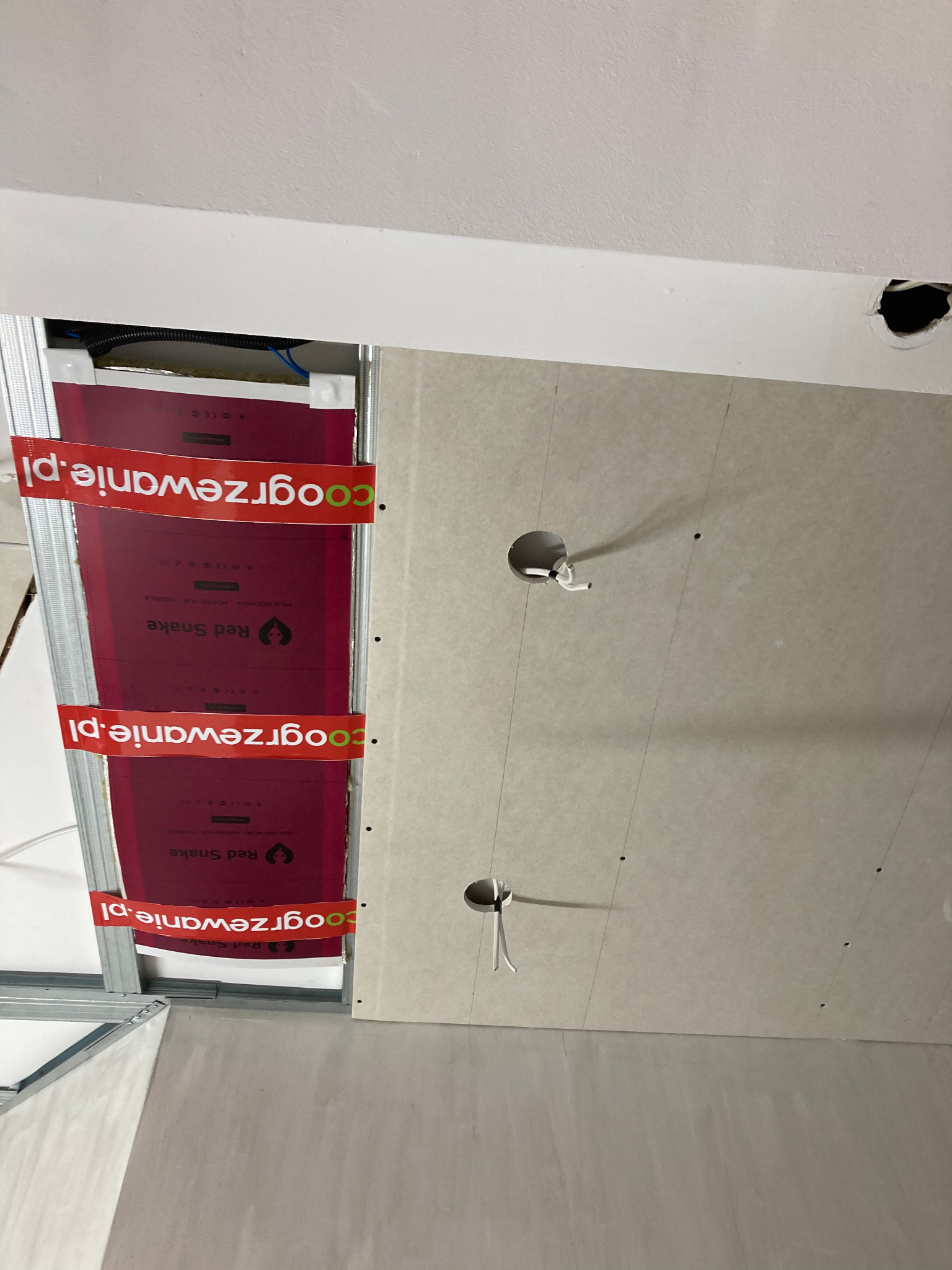 Montaż sufitu podwieszanego z płyt karton-gips: widoczne profile, izolacja termiczna Red Snake i otwory na oświetlenie. Etap prac wykończeniowych.