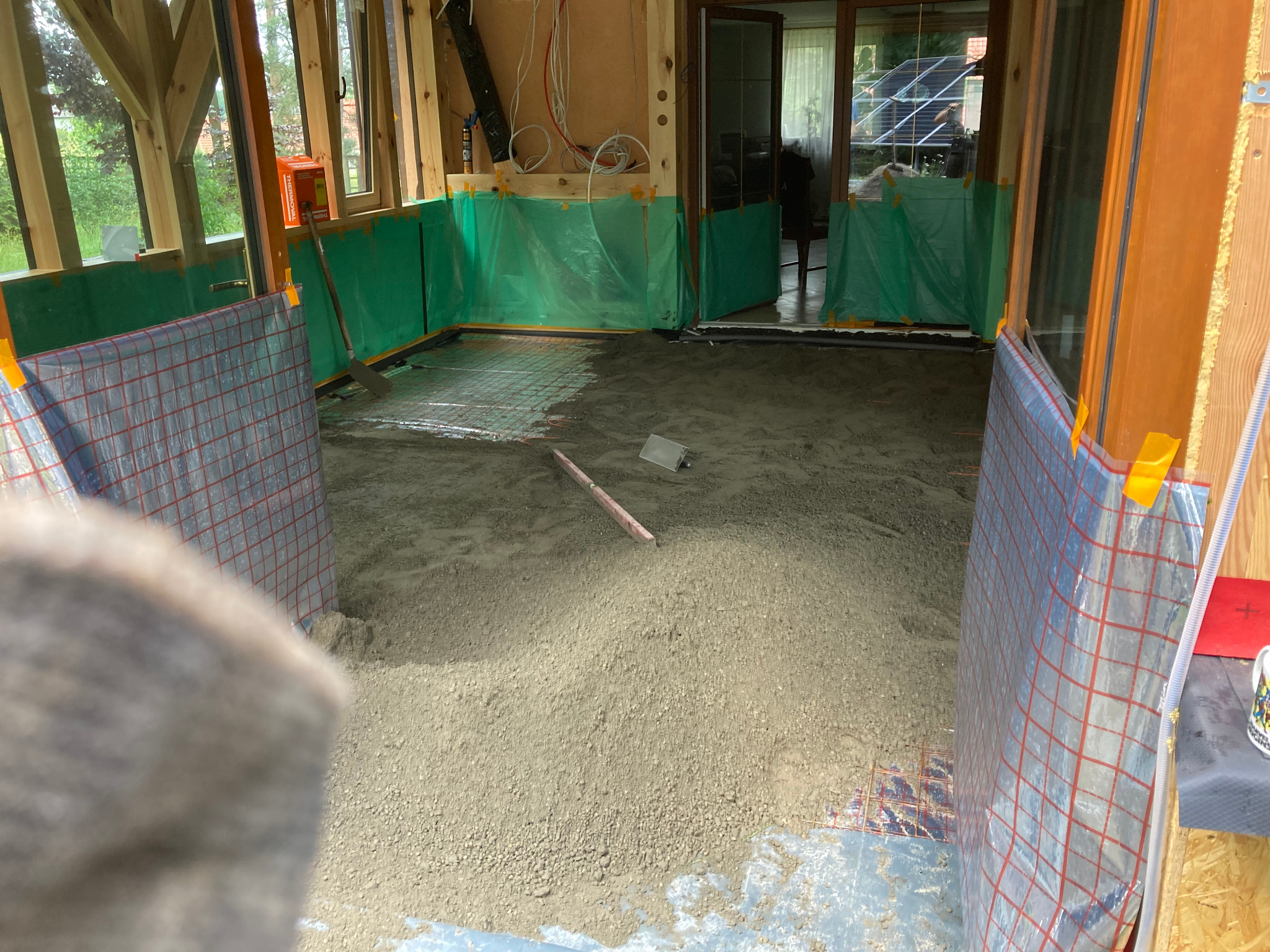 Przygotowanie podłoża pod wylewkę w nowo budowanym pomieszczeniu z drewnianą konstrukcją. Widoczna siatka zbrojeniowa i folia ochronna na ścianach.