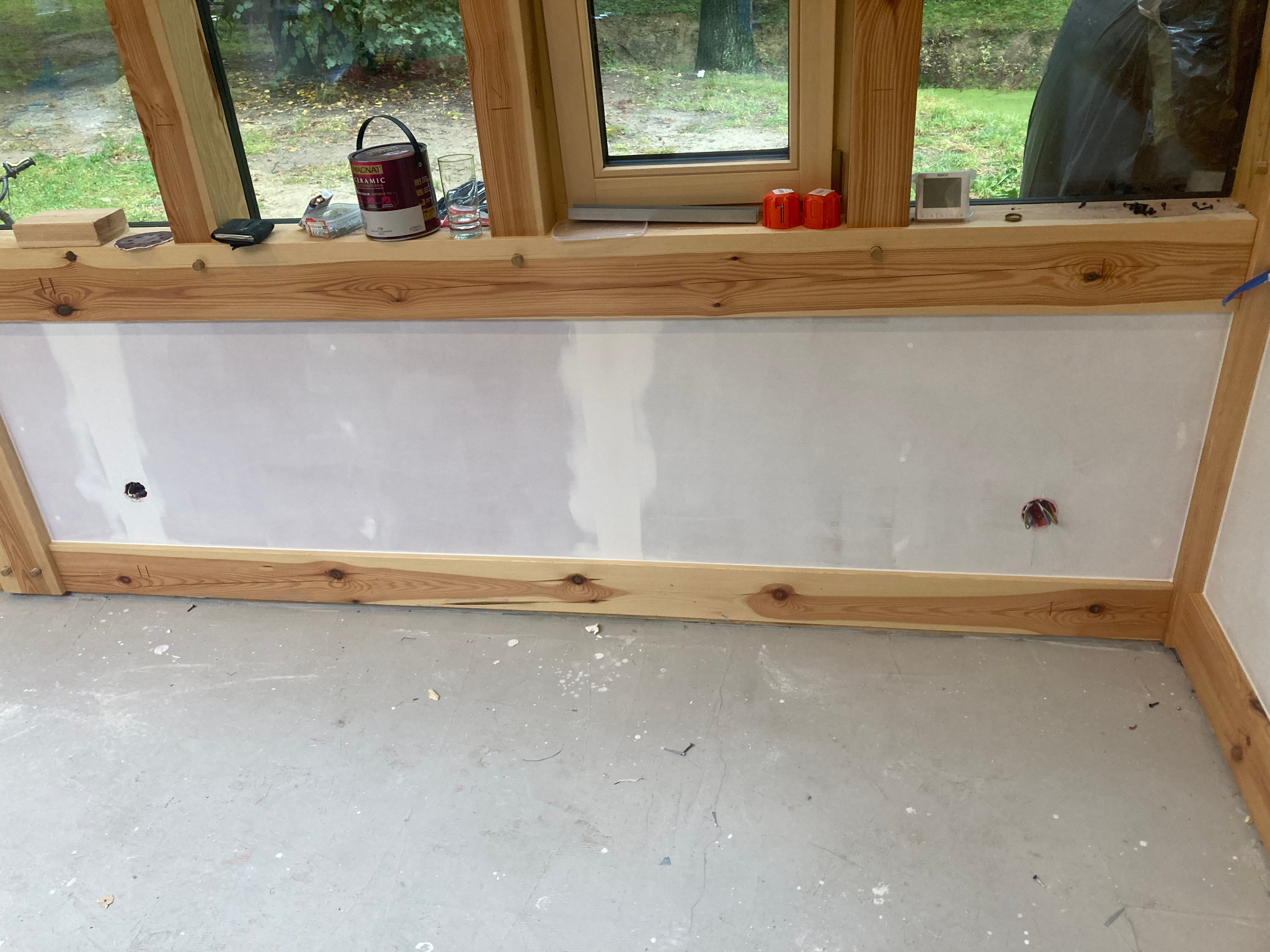 Fragment ściany z płyt karton-gips, drewniana rama, widoczne puszki elektryczne i narzędzia na parapecie. Etap szpachlowania, surowy stan wykończenia.