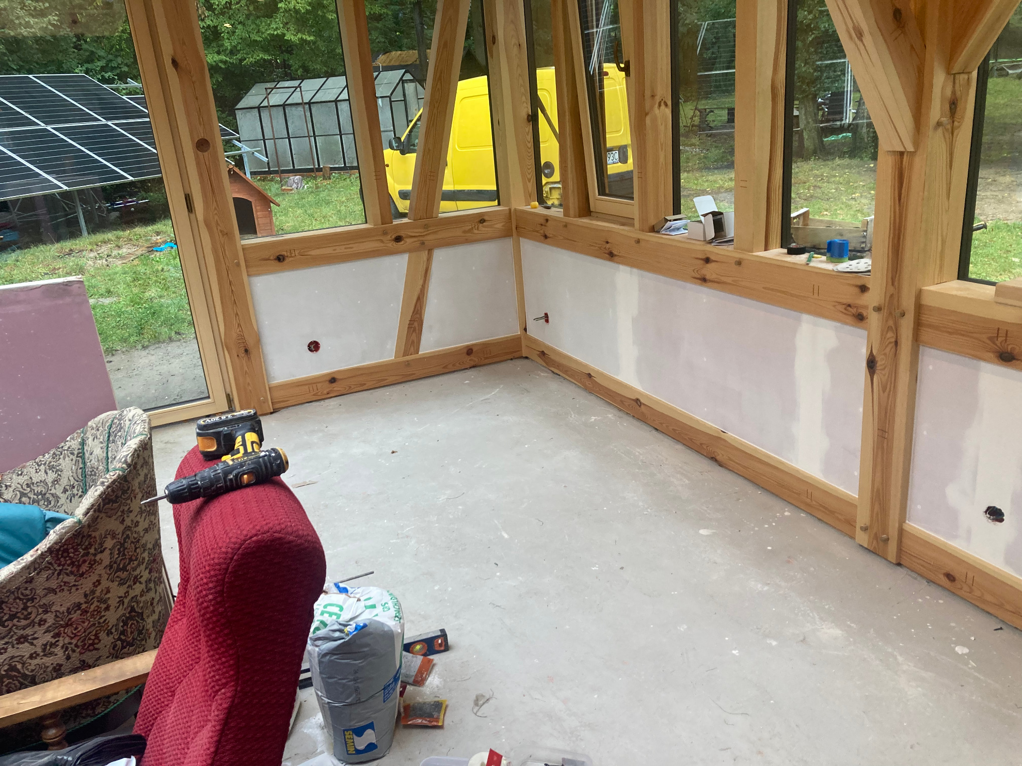 Wnętrze w trakcie wykańczania w Świdnicy: drewniana konstrukcja, częściowo wykończone ściany, narzędzia i materiały budowlane. Widok na zewnątrz przez okna.