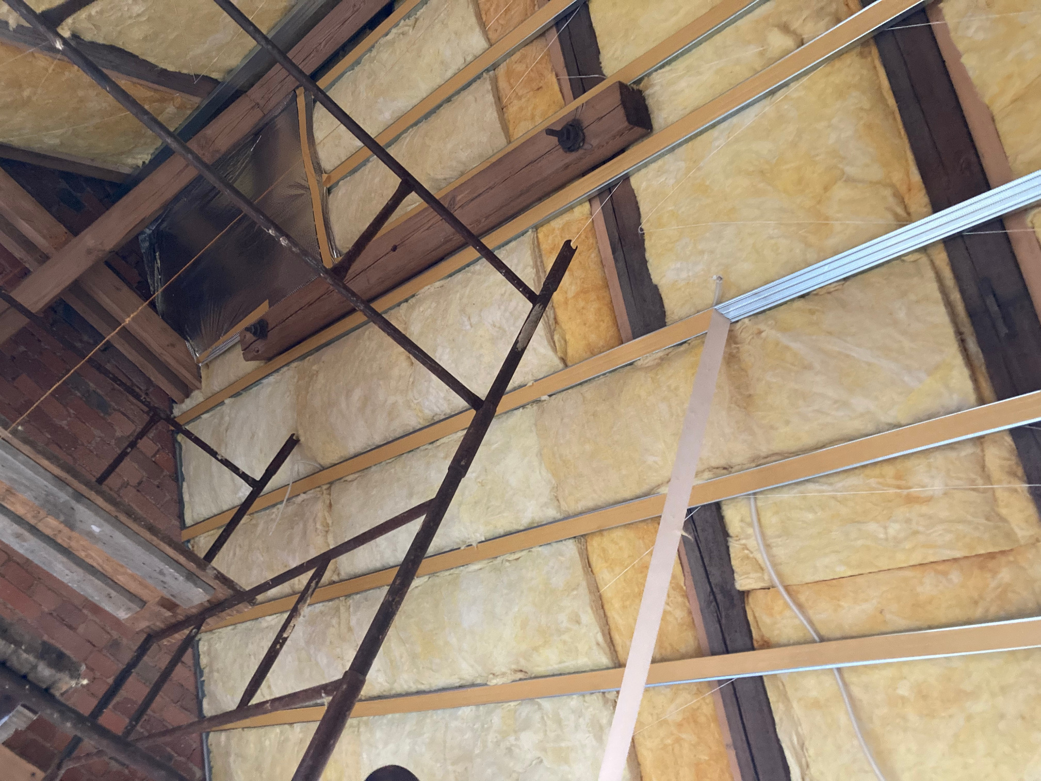 Ocieplenie poddasza wełną mineralną, widoczne drewniane i metalowe elementy konstrukcyjne oraz drabina. Prace wykończeniowe w trakcie realizacji.