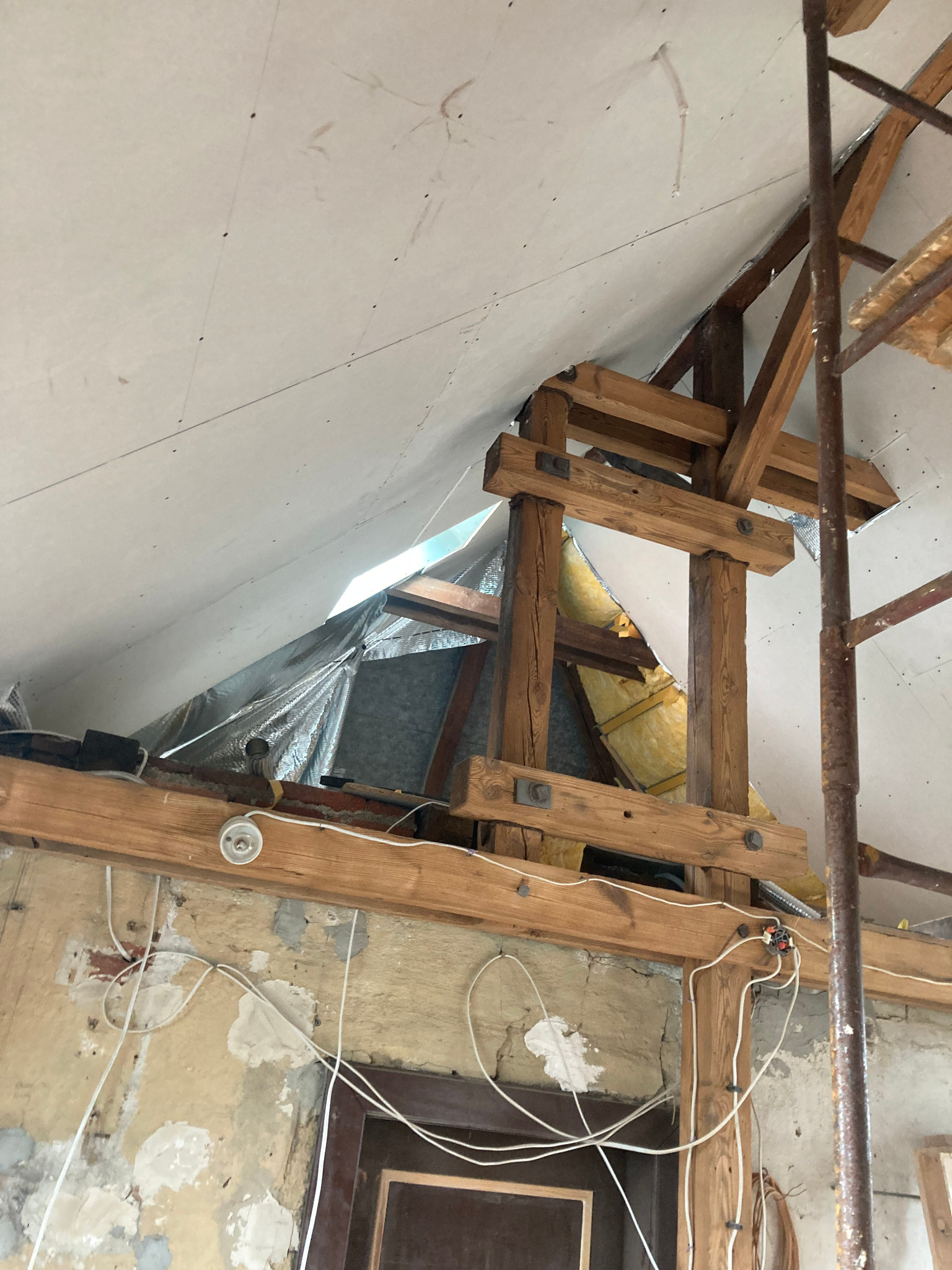 Poddasze w trakcie adaptacji: widoczne drewniane belki, izolacja, płyty karton-gips na suficie i fragment instalacji elektrycznej. Prace wykończeniowe w starym domu.