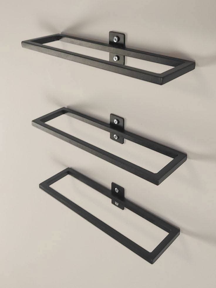 Trzy metalowe, prostokątne ramy, zamocowane do ściany za pomocą kwadratowych uchwytów z widocznymi śrubami, tworzące minimalistyczną dekorację ścienną.