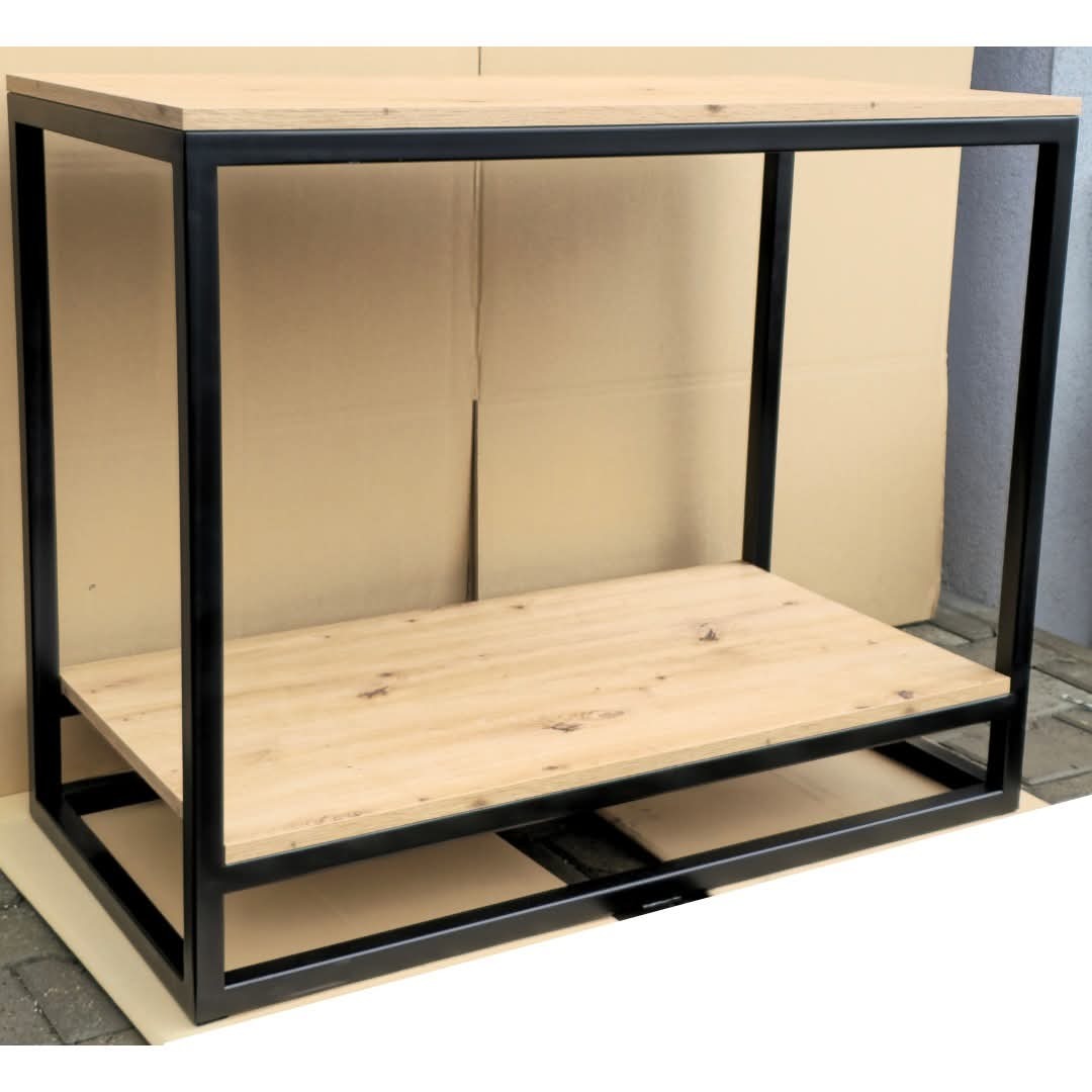 Stolik konsola z blatem z jasnego drewna i czarną, metalową ramą. Minimalistyczny design, widoczne spawy. Tło stanowi karton i fragment chodnika.