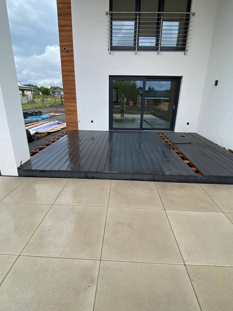 Montaż tarasu z desek kompozytowych na betonowej wylewce, widok z góry. Częściowo ułożone deski w kolorze grafitowym. Nowoczesna architektura domu w tle.