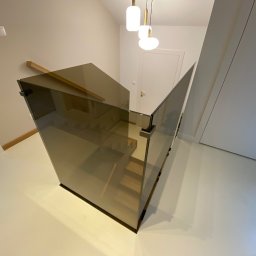 Kamil Wojciechowski - Nowoczesna, brązowa balustrada ze szkła na schodach w jasnym wnętrzu. Widok z góry, minimalistyczny design, eleganckie wykończenie.