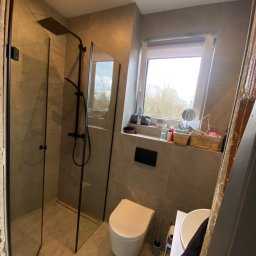 Kamil Wojciechowski - Nowoczesna łazienka z kabiną prysznicową typu walk-in z czarnymi profilami, toaletą i umywalką. Szare płytki imitujące marmur na ścianach i podłodze.