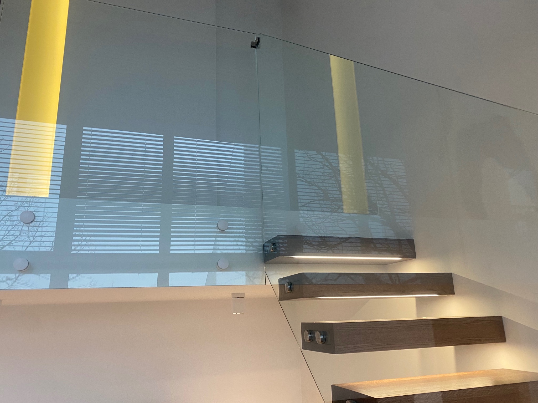 Szklana balustrada schodowa z drewnianymi stopniami podświetlonymi LED, widok z dołu, nowoczesny design.