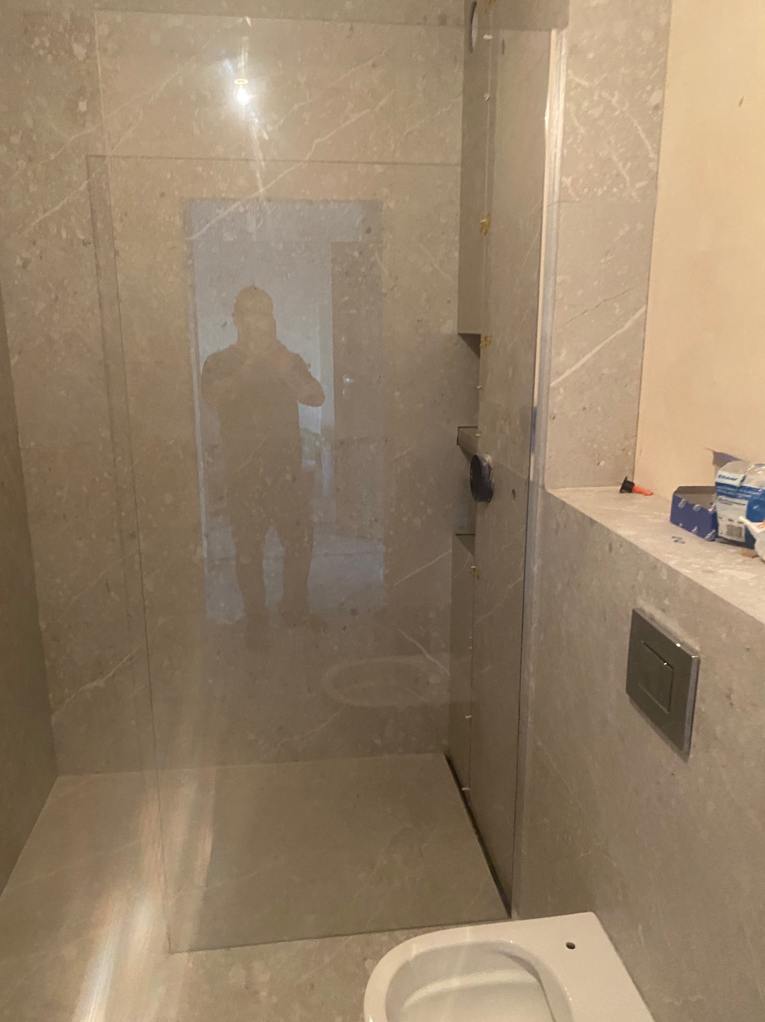 Wykończona kabina prysznicowa z szarego marmuru z widocznym odbiciem osoby robiącej zdjęcie. Minimalistyczny design, nowoczesne wykończenie łazienki.