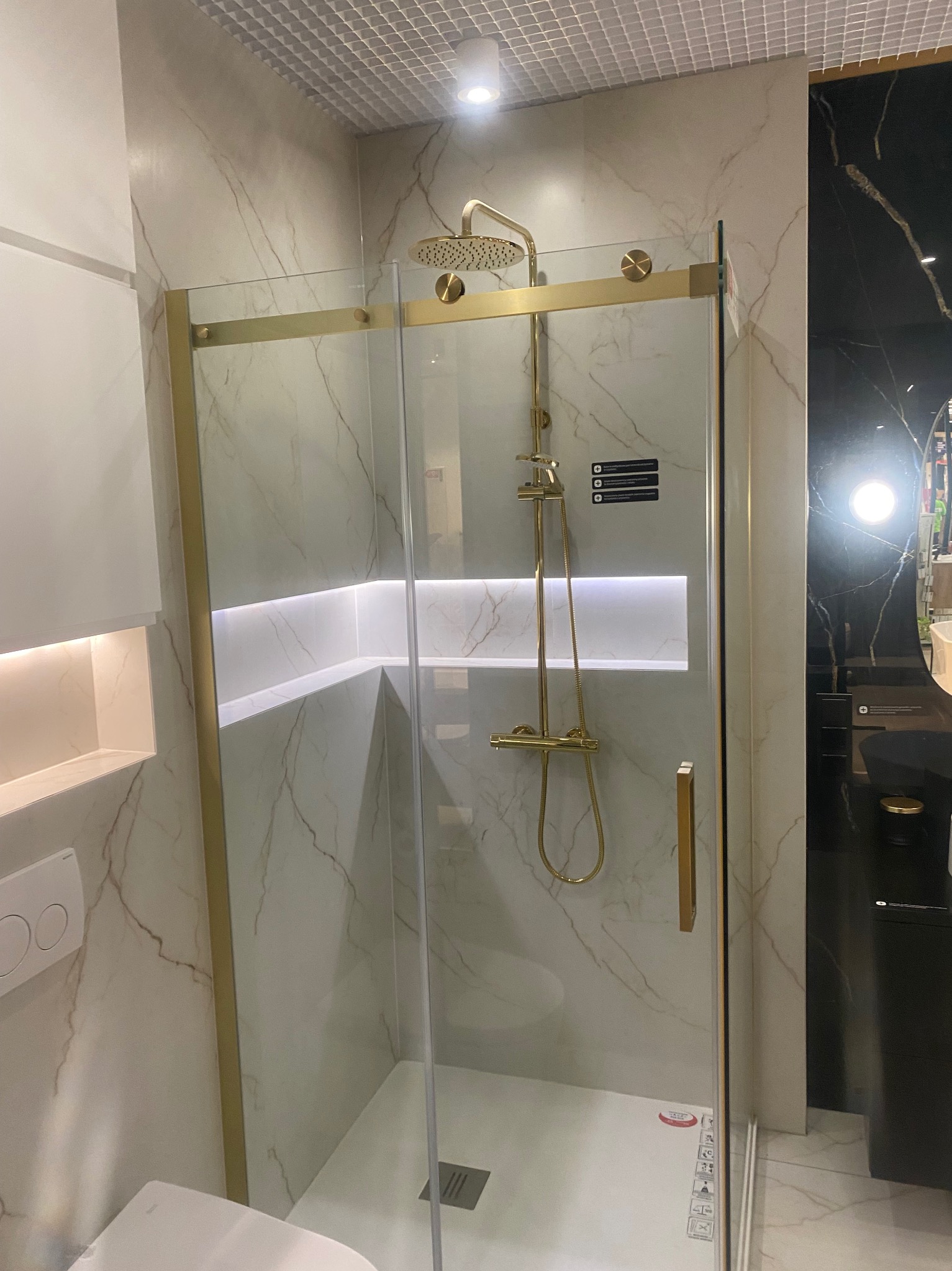 Kabina prysznicowa ze złotymi detalami i deszczownicą, marmurowe ściany z podświetleniem LED, nowoczesna aranżacja łazienki.