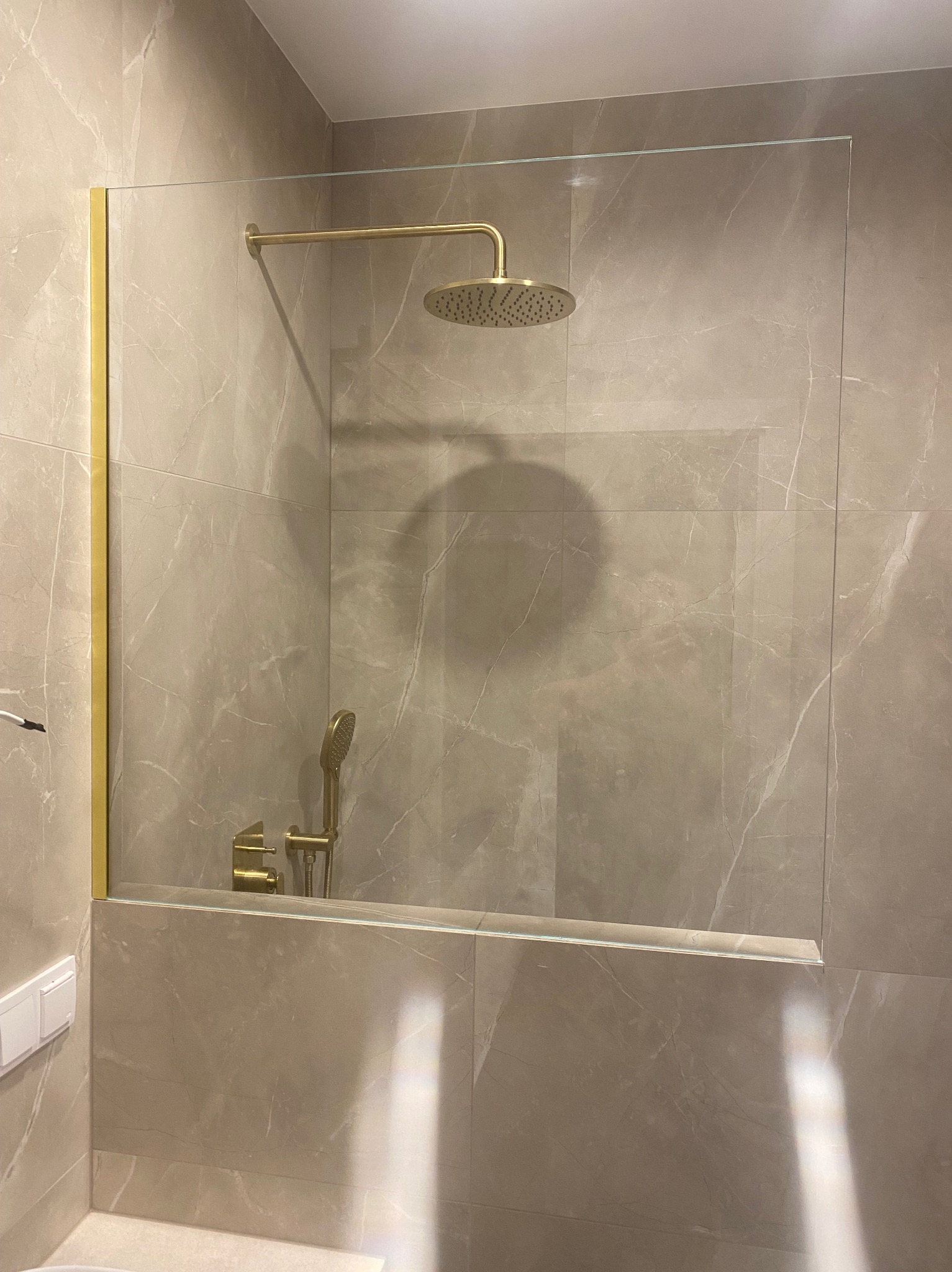 Beżowa łazienka z kabiną prysznicową ze szkła, złote wykończenia armatury i ramy kabiny. Minimalistyczny design, marmurowe płytki.