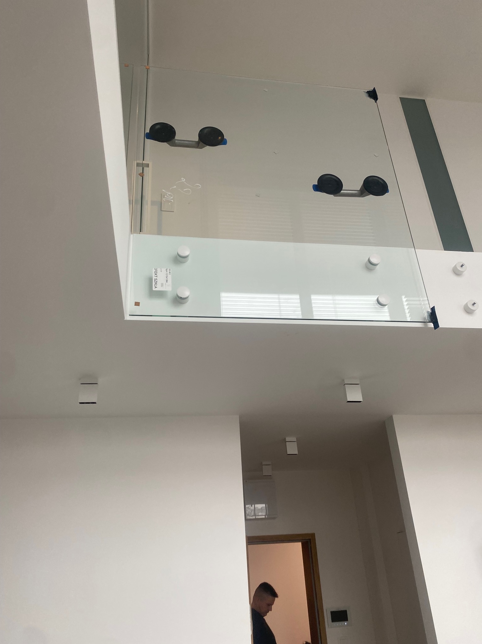 Szklana balustrada zamontowana na antresoli, widoczne przyssawki montażowe i mocowania punktowe. Minimalistyczny design, białe ściany, nowoczesne oświetlenie.