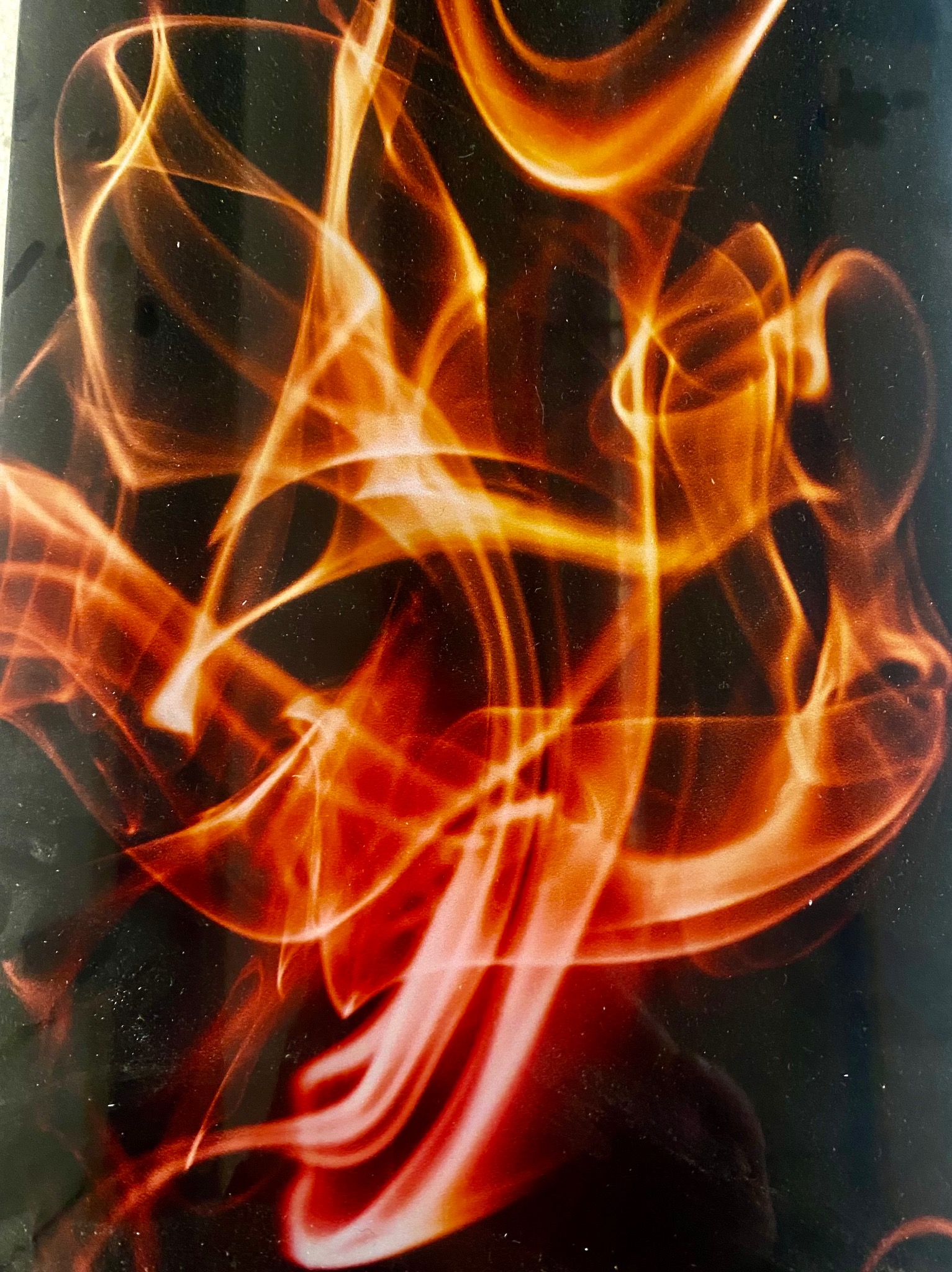 Abstrakcyjna gra światła na szklanej powierzchni, tworząca dynamiczne, płomienne wzory w odcieniach czerwieni i pomarańczy na ciemnym tle.