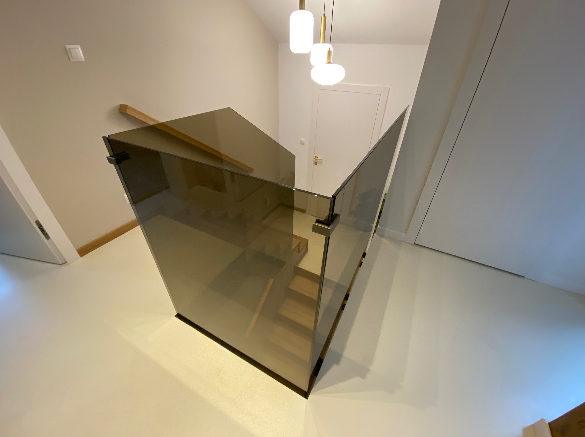 Nowoczesna, brązowa balustrada ze szkła na schodach w jasnym wnętrzu. Widok z góry, minimalistyczny design, eleganckie wykończenie.