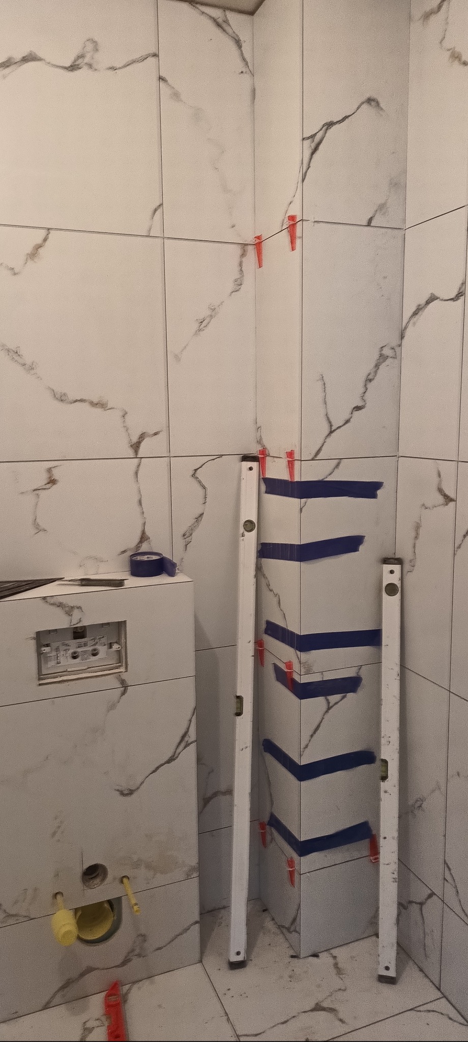 Montaż płytek imitujących marmur w łazience w Zgierzu. Widoczne poziomice, taśma maskująca i system poziomowania płytek. Prace glazurnicze w toku.