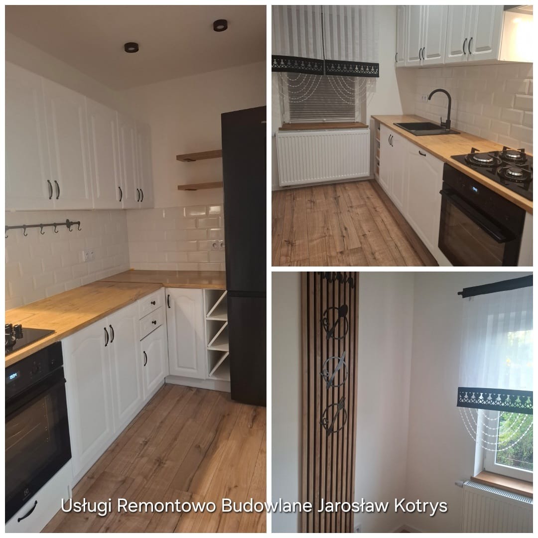 Biała kuchnia po remoncie z drewnianym blatem, płytkami typu metro i czarnymi akcentami, w tym lodówka i armatura. Widoczne drewniane półki i dekoracyjny panel ścienny.