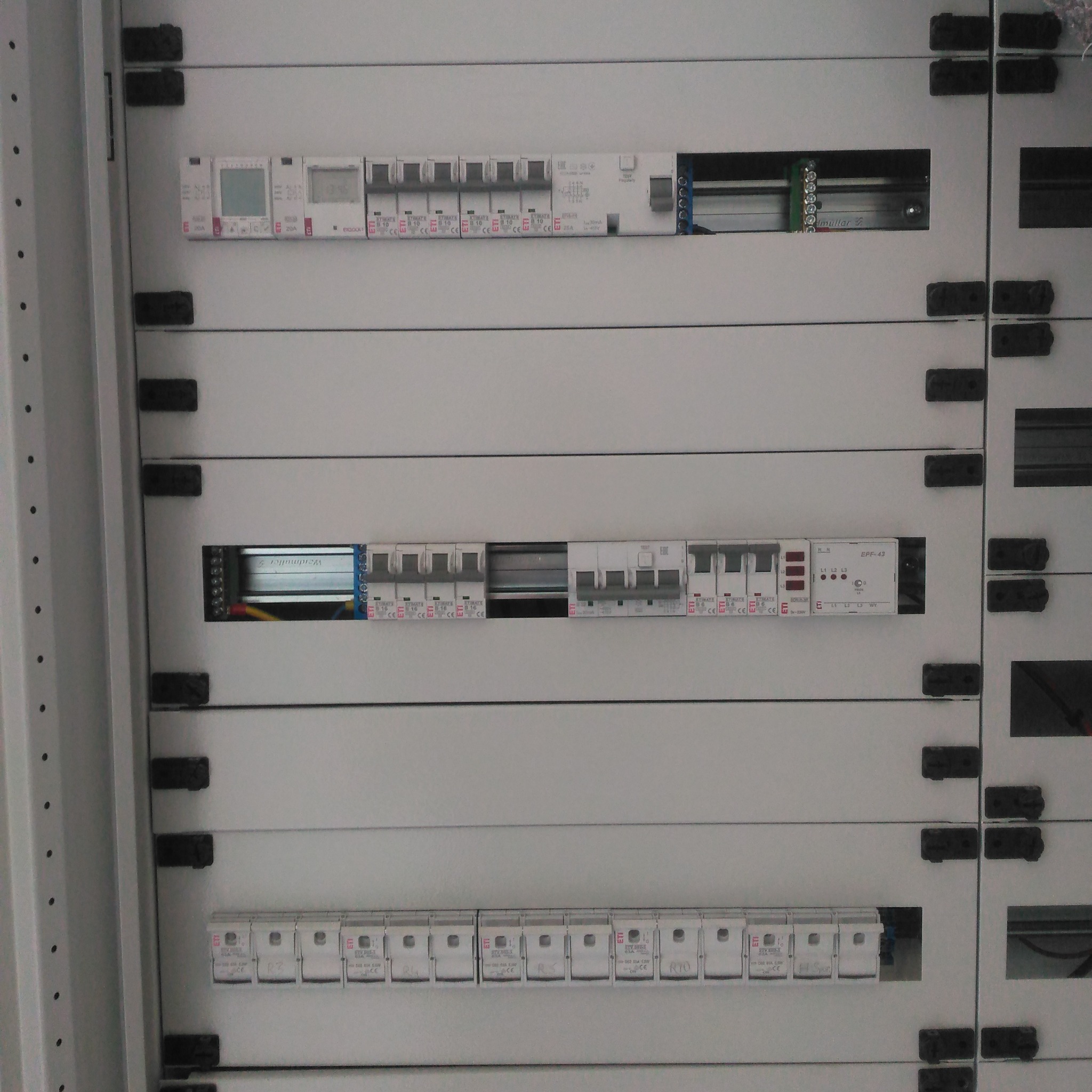 Rozdzielnica elektryczna z zamontowanymi bezpiecznikami i modułami, widok z bliska na szyny DIN i okablowanie wewnątrz szafy sterowniczej.