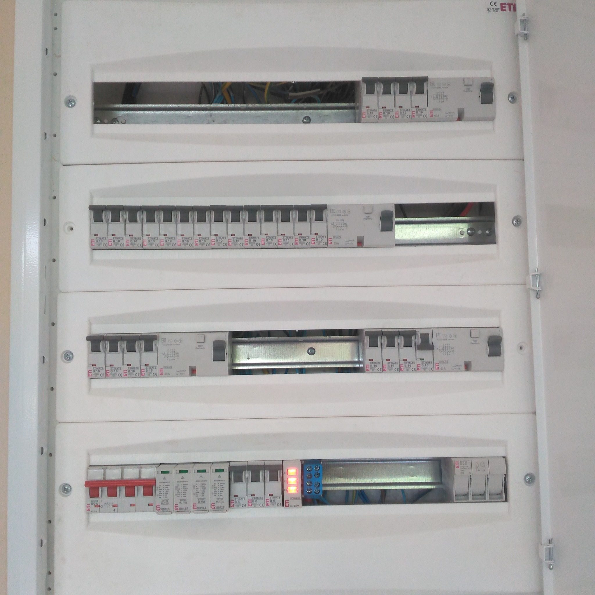 Rozdzielnica elektryczna z widocznymi bezpiecznikami i przewodami, zamontowana w białej obudowie. Widoczne oznaczenia producenta ETI.