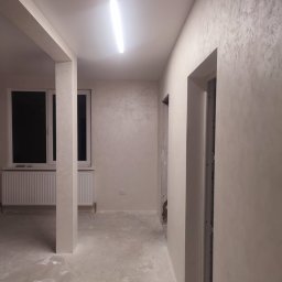 VOLODYMYR LUTSENKO - Wykończone wnętrze po remoncie: ściany z dekoracyjną fakturą, pomalowane na jasny kolor, widoczne okno i fragment kolumny. Na podłodze folia ochronna.