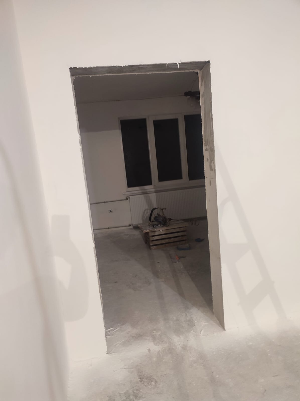 Surowy otwór drzwiowy w trakcie prac wykończeniowych w Gdańsku. Widoczne ślady szpachlowania i przygotowania do malowania. W tle okno i narzędzia na podłodze.