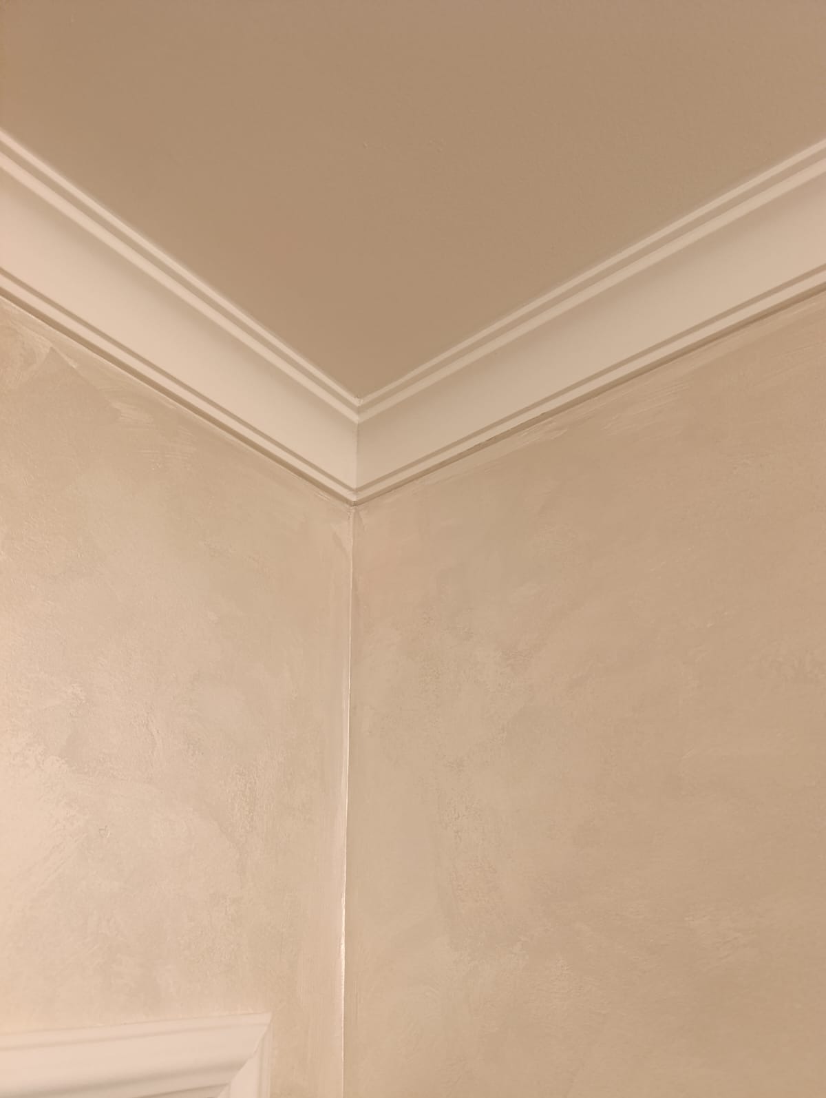 Jasny narożnik pokoju po gładzi, z dekoracyjną listwą przysufitową. Ściany w odcieniach beżu, z delikatną fakturą. Widoczne subtelne przejścia kolorystyczne.