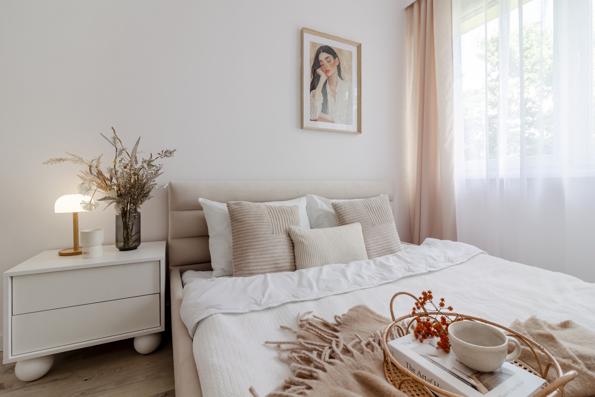 Jasna sypialnia w Kiełczowie z beżowym łóżkiem, stolikiem nocnym z lampką i dekoracjami. Na ścianie grafika. Przytulny, minimalistyczny wystrój.