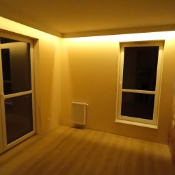 Warmińskie Domy PATRYK GICZEWSKI - Pokój po remoncie z oknem, drzwiami balkonowymi i grzejnikiem. Ściany pomalowane na beżowo, jedna ściana z efektem dekoracyjnym. Oświetlenie sufitowe.