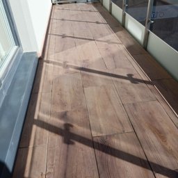 Warmińskie Domy PATRYK GICZEWSKI - Ułożona podłoga z paneli imitujących drewno na balkonie w Bartągu. Widoczne cienie konstrukcji balkonu. Jasne, naturalne światło.