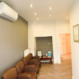 Warmińskie Domy PATRYK GICZEWSKI - Klimatyzacja na ścianie z tapetą w odcieniach szarości, brązowe fotele w poczekalni, oświetlenie punktowe i certyfikat w ramce na ścianie w tle.