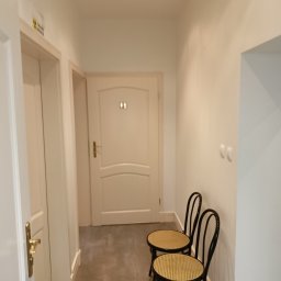Warmińskie Domy PATRYK GICZEWSKI - Jasny korytarz z dwiema krzesłami wiedeńskimi, prowadzący do drzwi z oznaczeniem toalet. Minimalistyczny design, szara podłoga, subtelne oświetlenie.