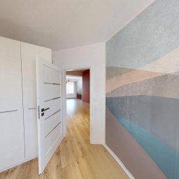 Warmińskie Domy PATRYK GICZEWSKI - Białe drzwi wewnętrzne z poziomymi zdobieniami, otwarte do wnętrza. Na ścianie dekoracyjna tapeta w poziome pasy. Widok na parkiet i dalsze pomieszczenia.