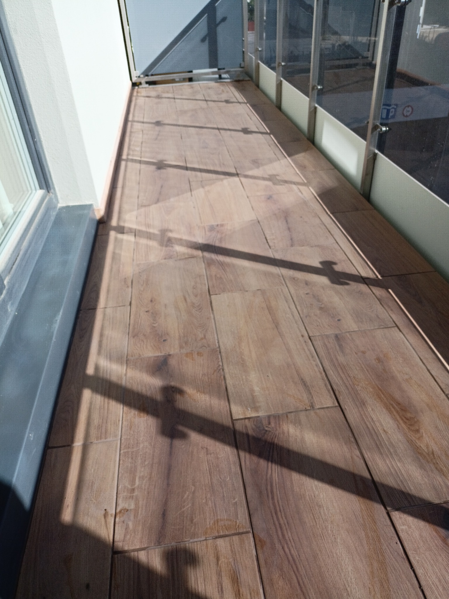 Ułożona podłoga z paneli imitujących drewno na balkonie w Bartągu. Widoczne cienie konstrukcji balkonu. Jasne, naturalne światło.