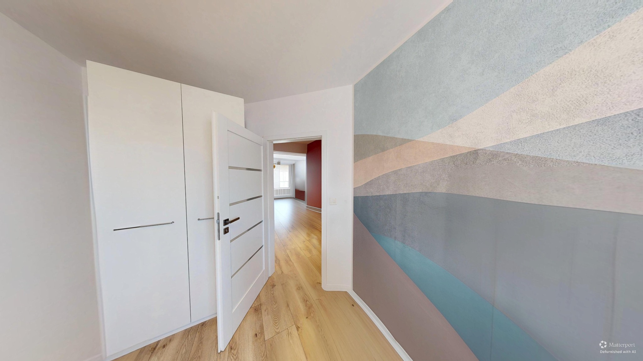 Białe drzwi wewnętrzne z poziomymi zdobieniami, otwarte do wnętrza. Na ścianie dekoracyjna tapeta w poziome pasy. Widok na parkiet i dalsze pomieszczenia.