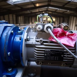AutomatykaElektrykaDruk3D Zbigniew Obręczarek - Szczegółowe ujęcie silnika elektrycznego Innomotics z podłączonymi kablami, umieszczonego w hali przemysłowej z oknami dachowymi. Widoczne śruby i elementy mocujące.