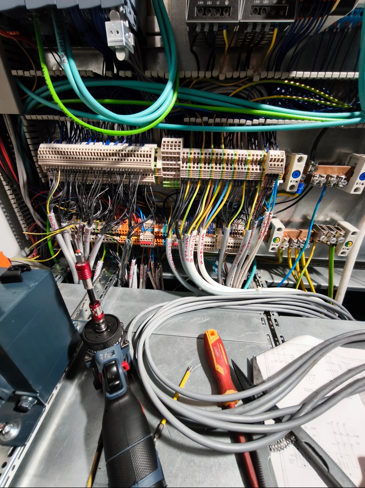 Rozdzielnica elektryczna w trakcie montażu: widoczne kable, listwy zaciskowe, narzędzia (wkrętarka, śrubokręt) i schemat. Przewody w różnych kolorach uporządkowane w szafie.