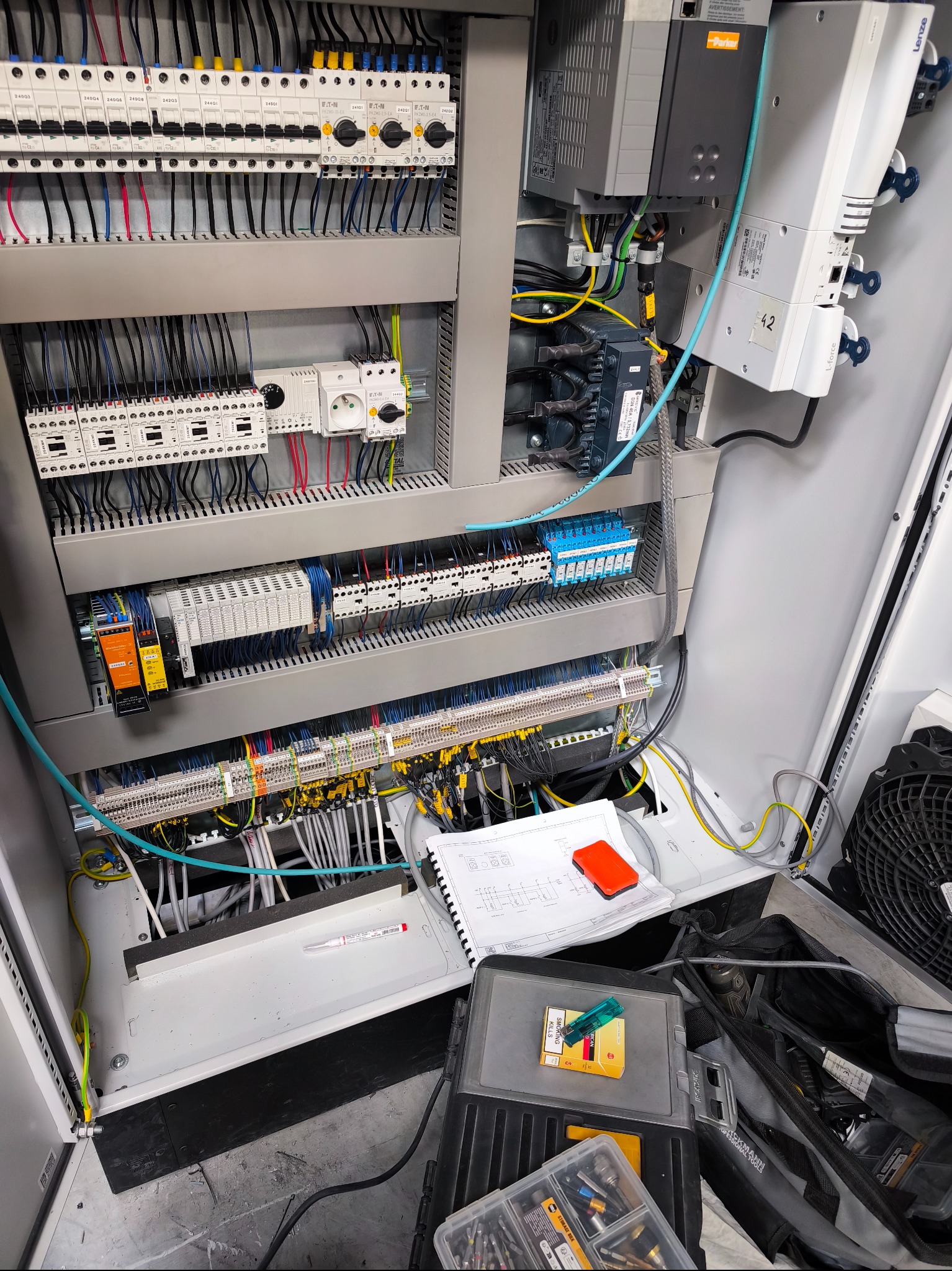 Rozbudowana szafa sterownicza z licznymi przewodami, bezpiecznikami i elementami automatyki. Widoczne narzędzia i schematy elektryczne sugerują prace instalacyjne.