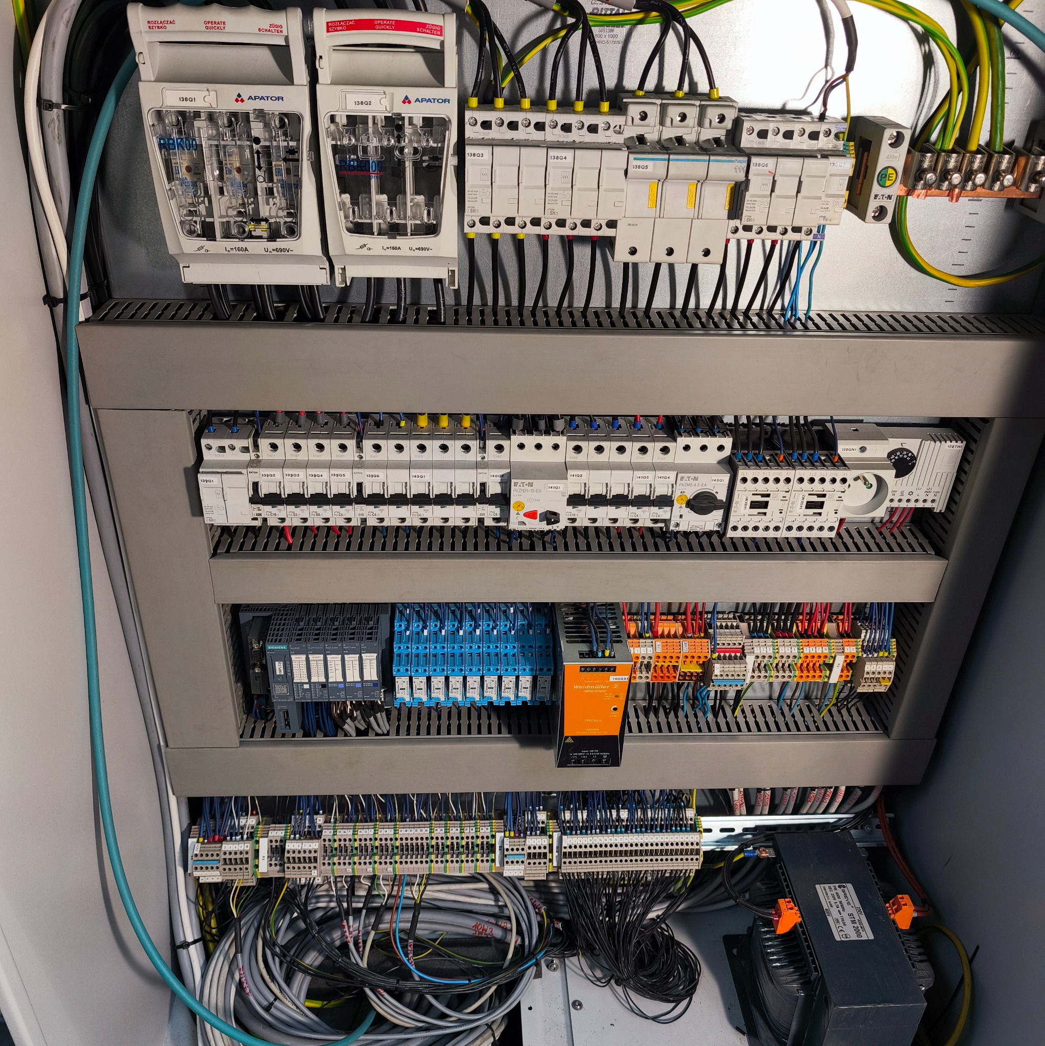 Rozbudowana szafa sterownicza z licznymi bezpiecznikami, przekaźnikami i okablowaniem. Widoczne elementy marki Apator i Weidmüller.