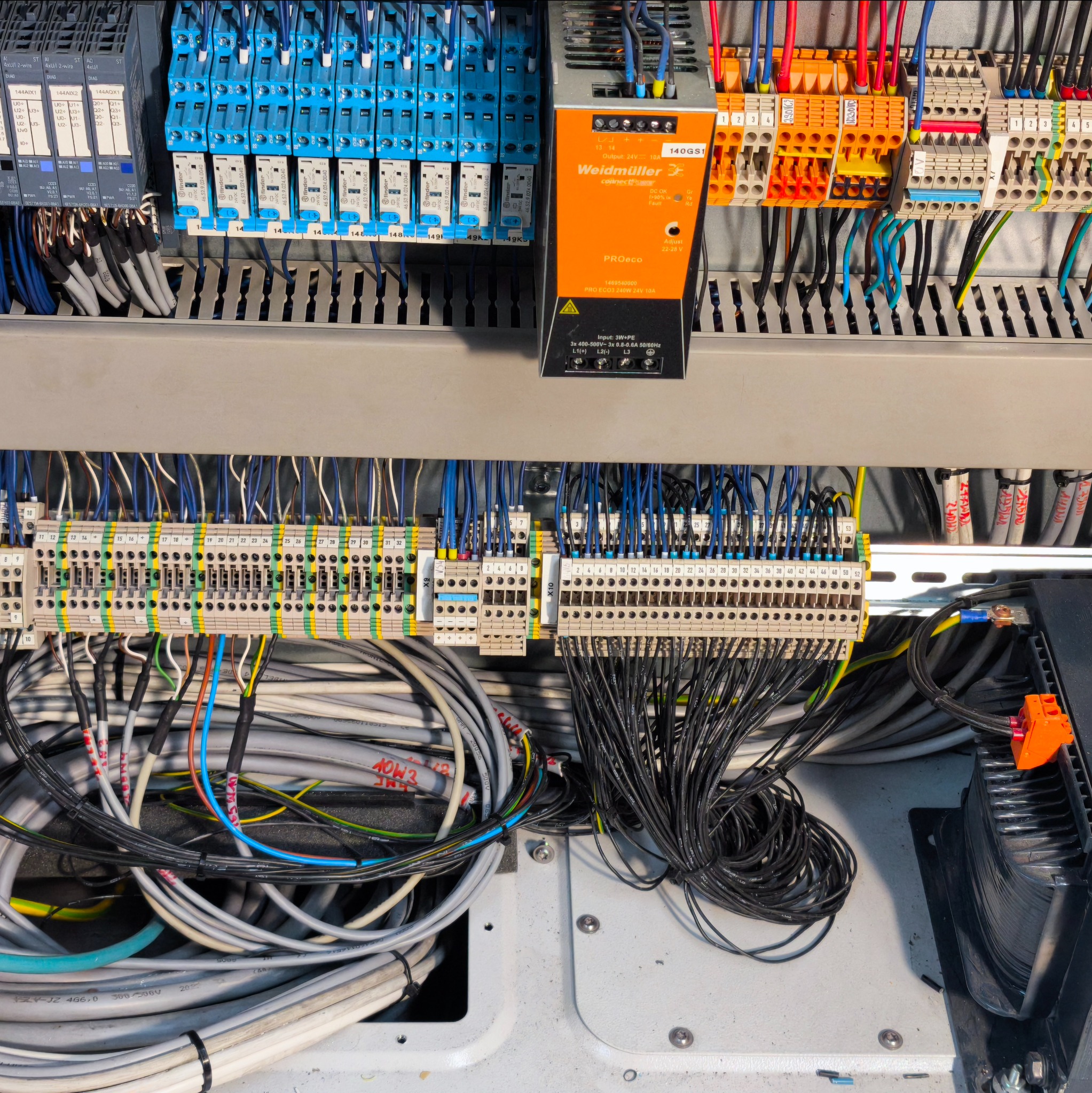 Rozbudowana szafa sterownicza z licznymi przekaźnikami, modułami Weidmüller i gęstą siecią przewodów w różnych kolorach, tworząca skomplikowany system elektryczny.