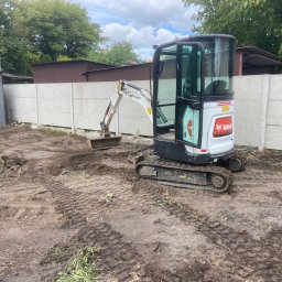 F.H.U. Marek Szwed - Mini koparka Bobcat na placu budowy, ślady opon w błocie, betonowe ogrodzenie w tle, częściowo oczyszczony teren. Prace ziemne w toku.
