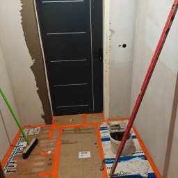 Przedsiębiorstwo Robót Budowlanych ART-DOM Artur Kuk - Montaż drzwi wewnętrznych w trakcie remontu. Widoczne przygotowane podłoże, poziomica i narzędzia. Ściany w trakcie wykończenia.