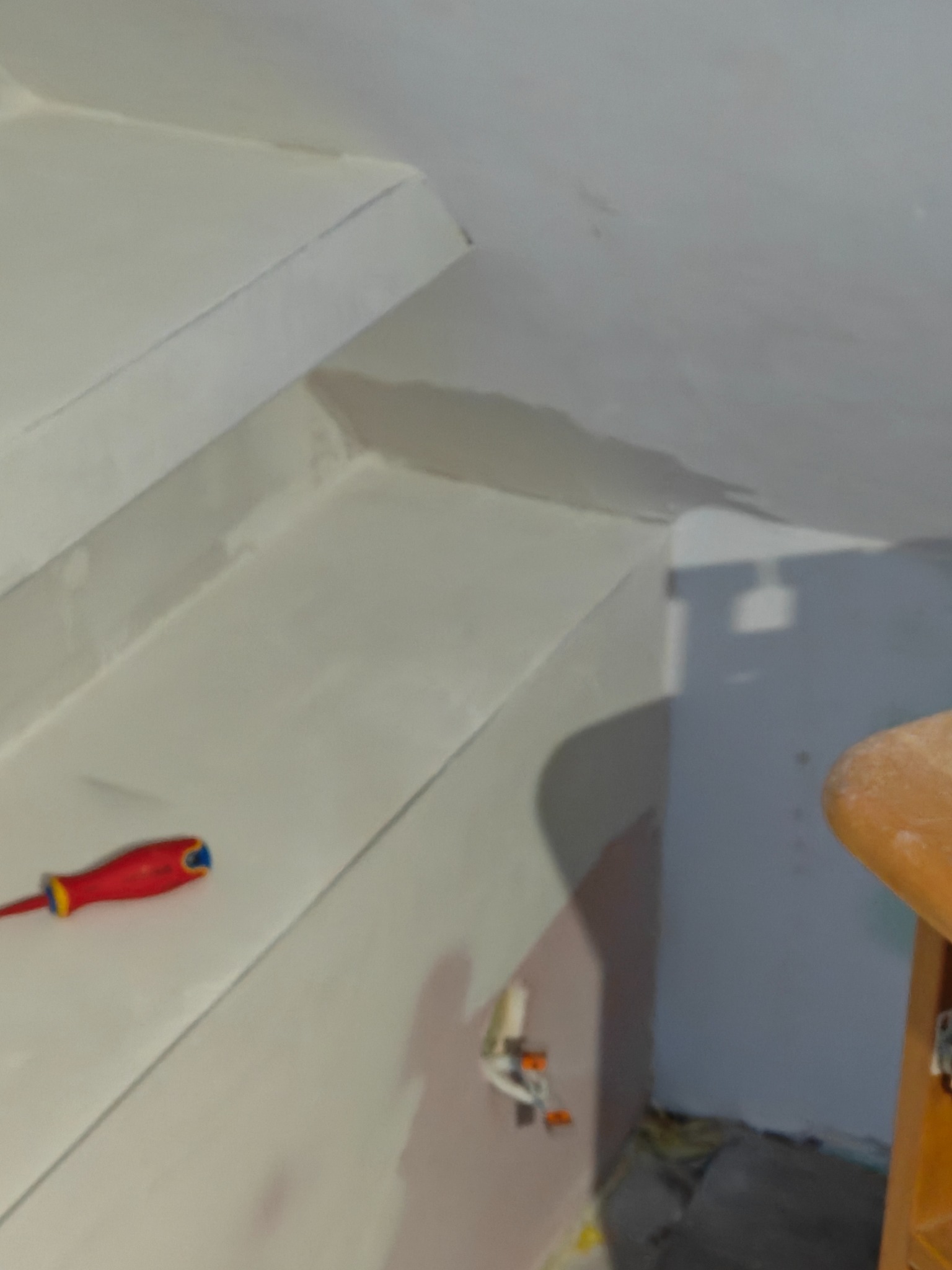 Wnętrze w trakcie szpachlowania: gładkie, białe ściany schodów, czerwono-żółty śrubokręt leżący na stopniu, widoczne kable elektryczne w ścianie.