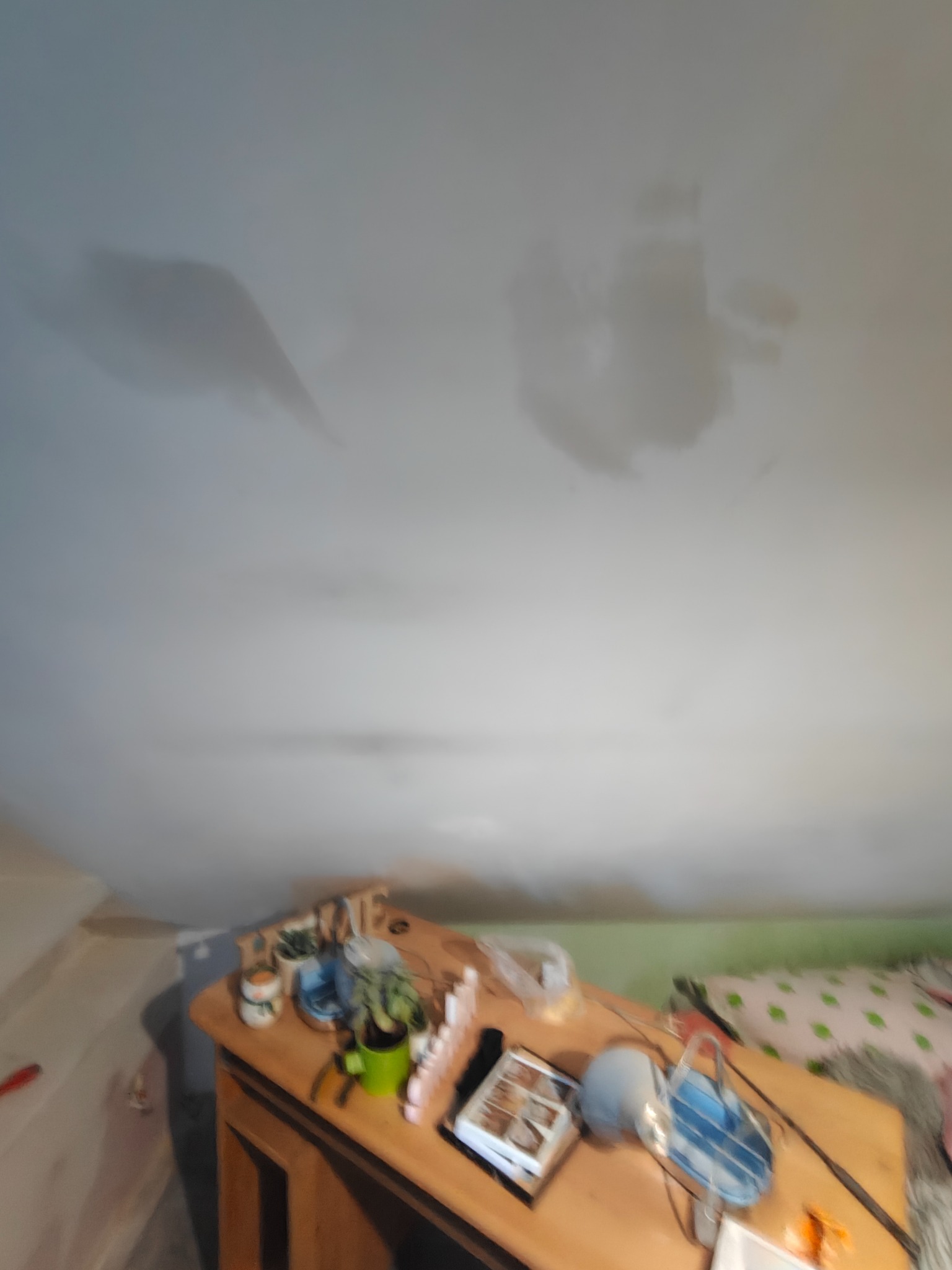 Niejednolita powierzchnia sufitu z widocznymi plamami, sugerującymi potencjalne problemy z wilgocią. Na pierwszym planie drewniany blat z dekoracjami.