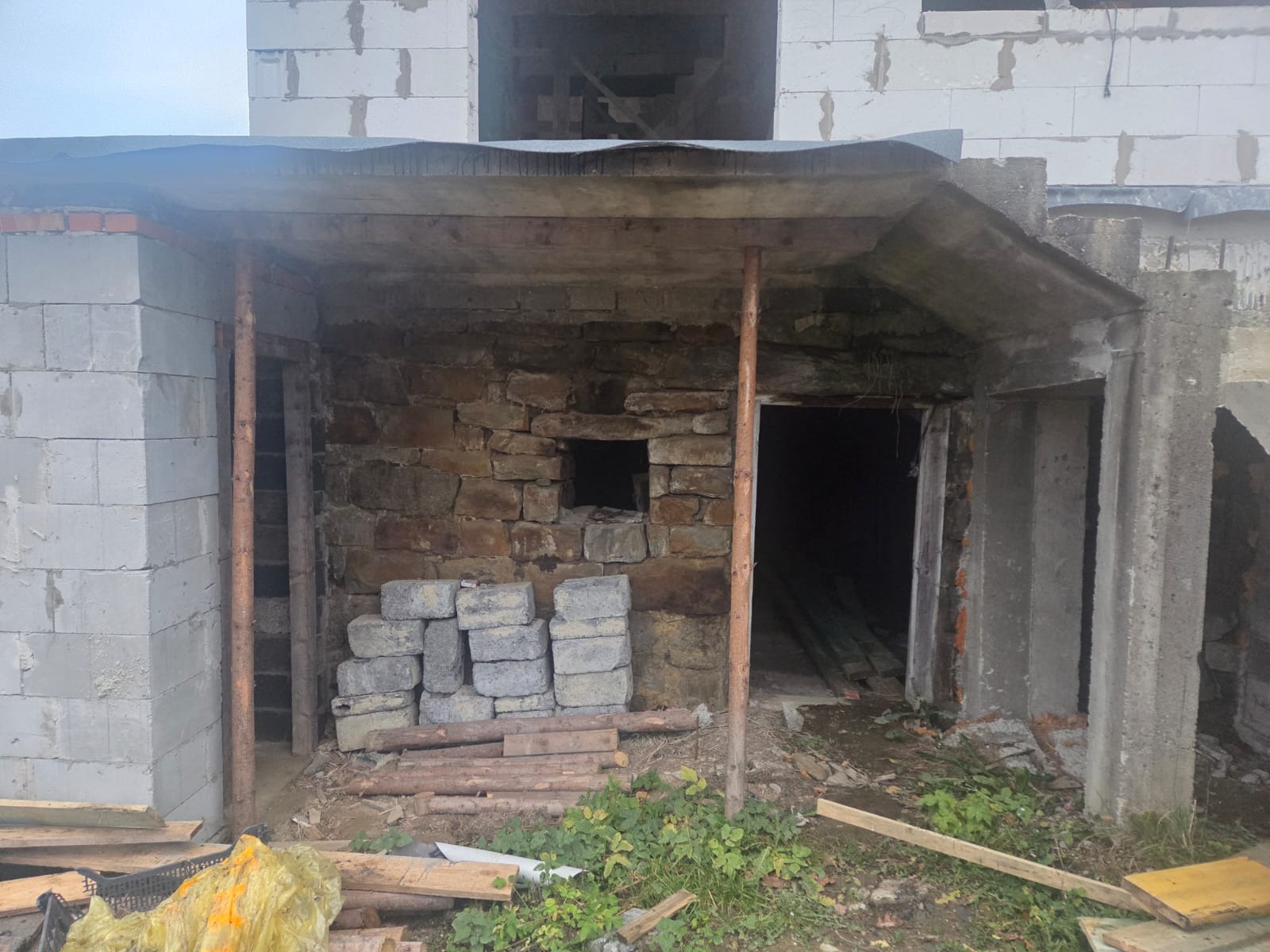 Surowy stan budynku w trakcie budowy: ściany z kamienia i bloczków, drewniane podpory, widoczne materiały budowlane. Etap prac murarskich.