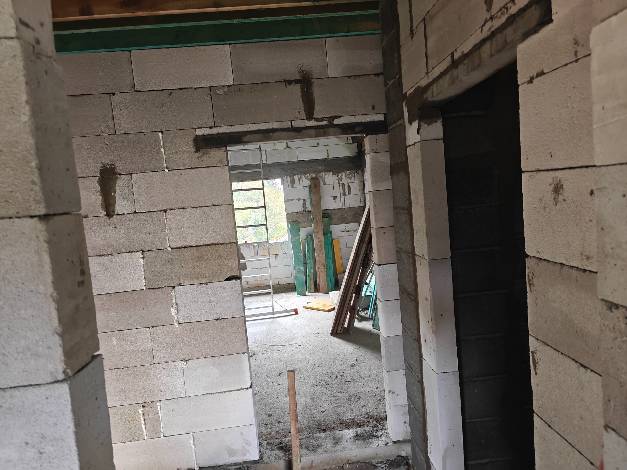 Surowy stan domu w budowie: ściany z betonu komórkowego, widoczne otwory drzwiowe i okienne, drabina w tle. Wnętrze w trakcie wznoszenia.