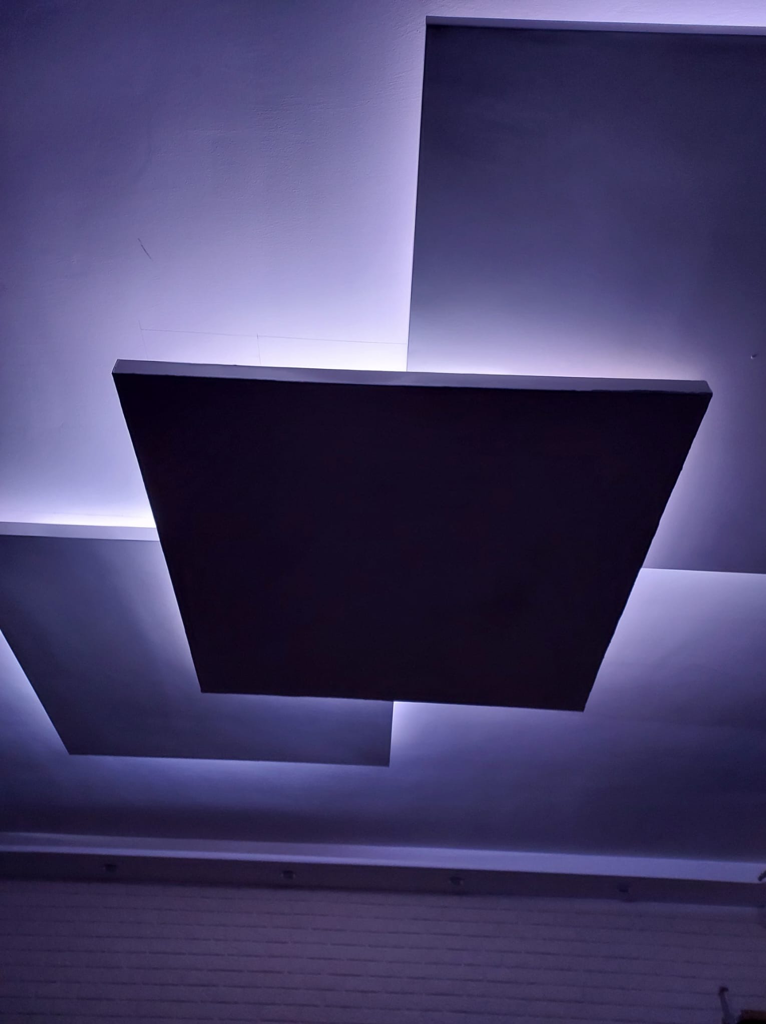 Nowoczesny sufit podwieszany z kwadratowymi panelami i subtelnym, fioletowym podświetleniem LED, tworzący unikalny efekt wizualny.