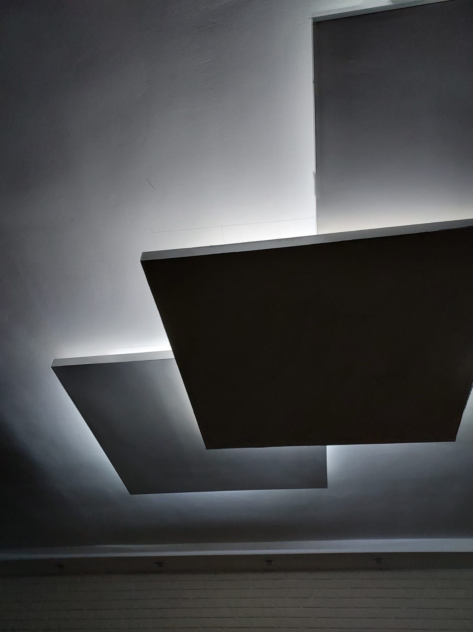 Nowoczesny sufit podwieszany z oświetleniem LED, tworzący geometryczny wzór. Minimalistyczny design z subtelnym światłem podkreślającym kształty.