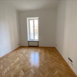 Yaroslav Nakonechnyi - Pusty pokój po remoncie z parkietem w jodełkę, świeżo pomalowanymi ścianami i oknem z grzejnikiem. Widoczne gniazdka elektryczne bez osprzętu.