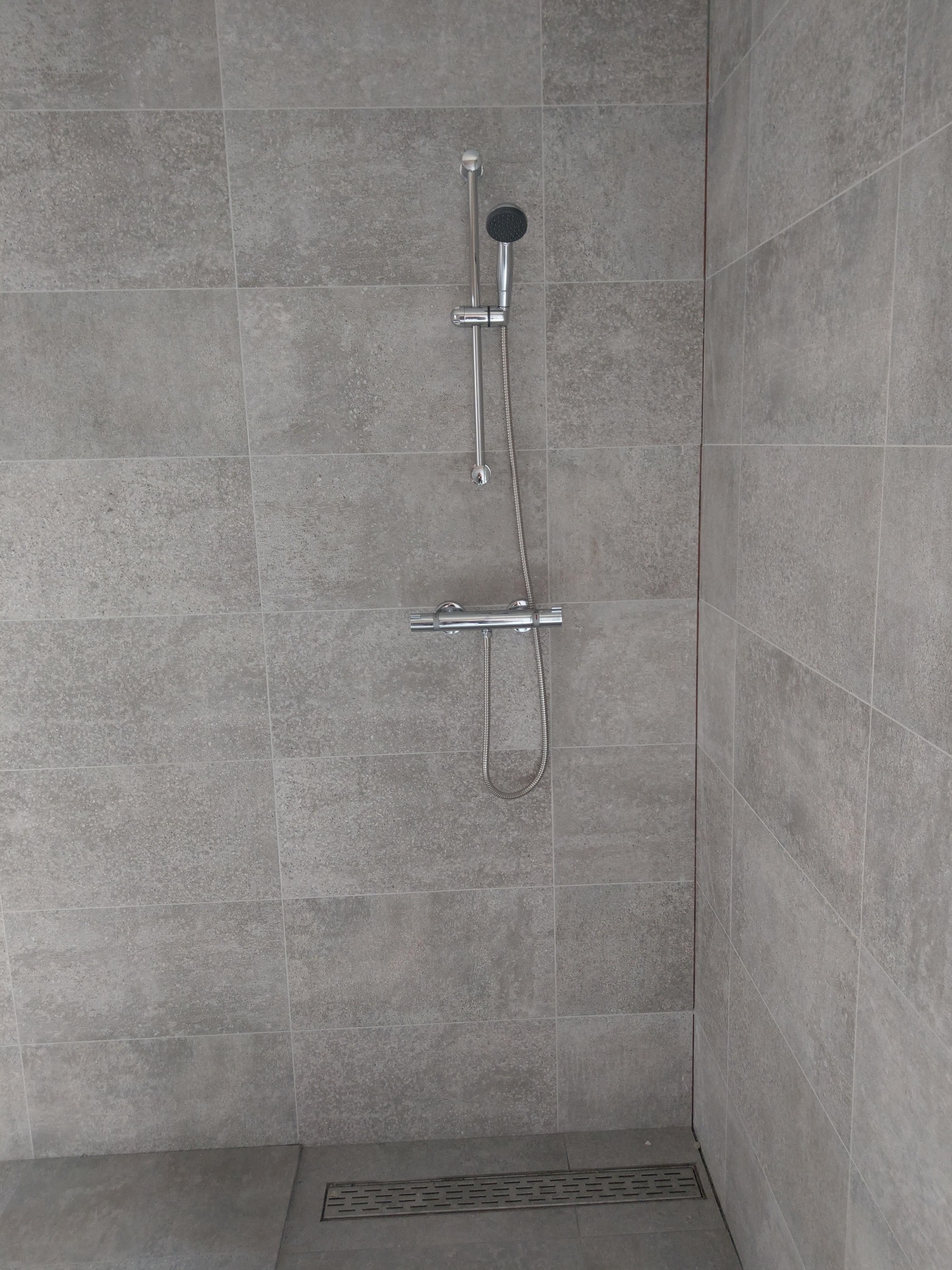 Nowoczesna kabina prysznicowa z szarymi płytkami i chromowaną armaturą. Minimalistyczny design z odpływem liniowym w podłodze.